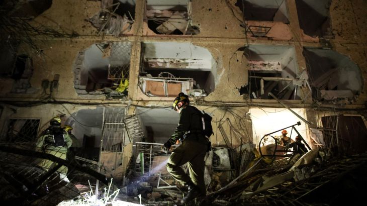 Emergency responders search through the rubble of a damaged building at night