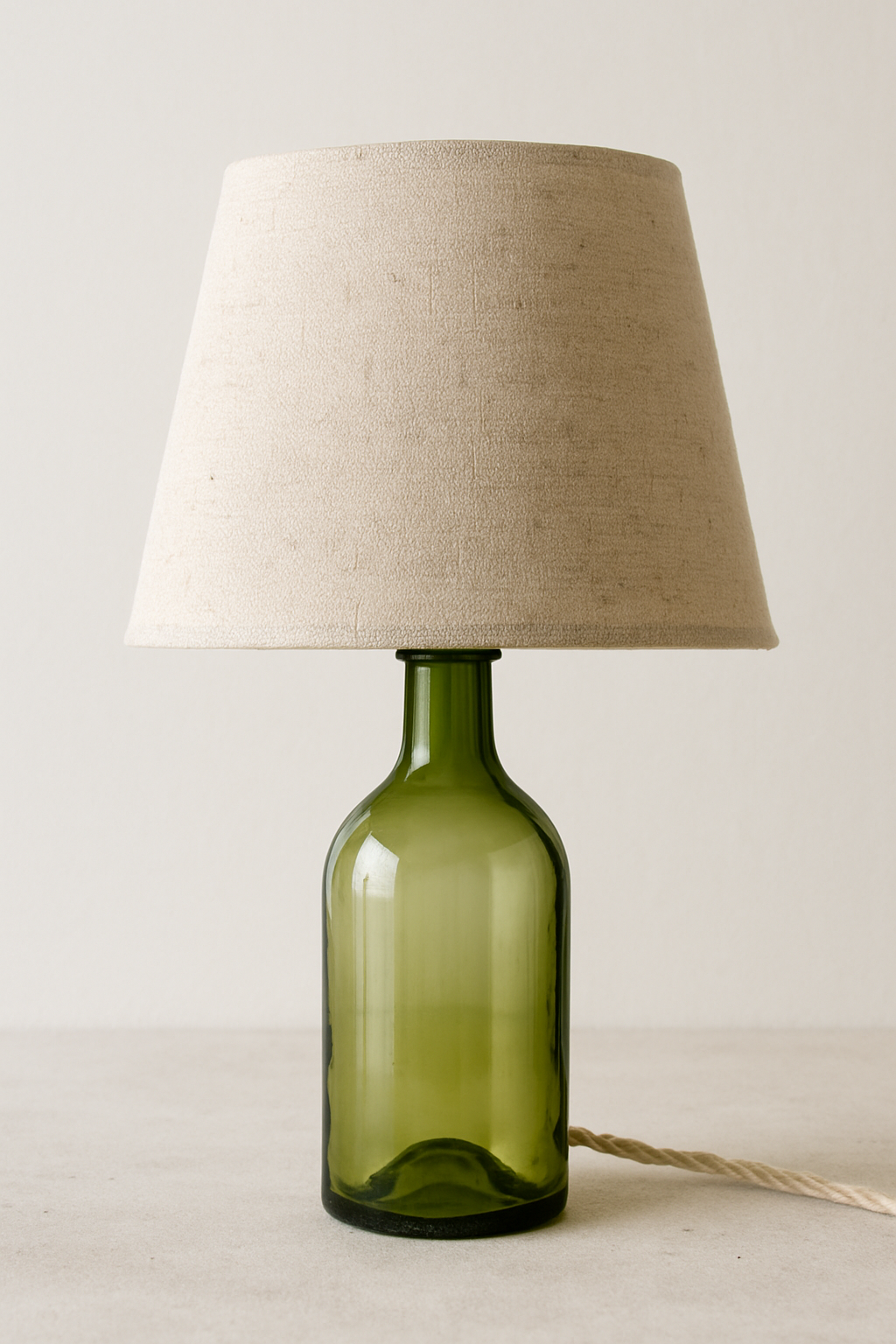 Imagem de uma Luminária de mesa com base feita de garrafa de vidro de vinho cortada e cúpula de tecido de linho cru.