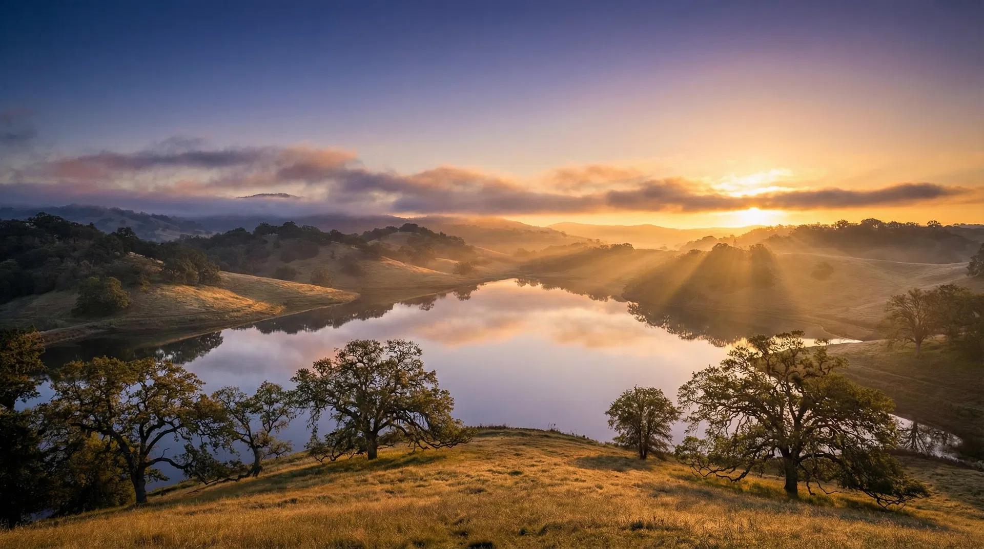 Sunrise over a serene lake surrounded by golden hills