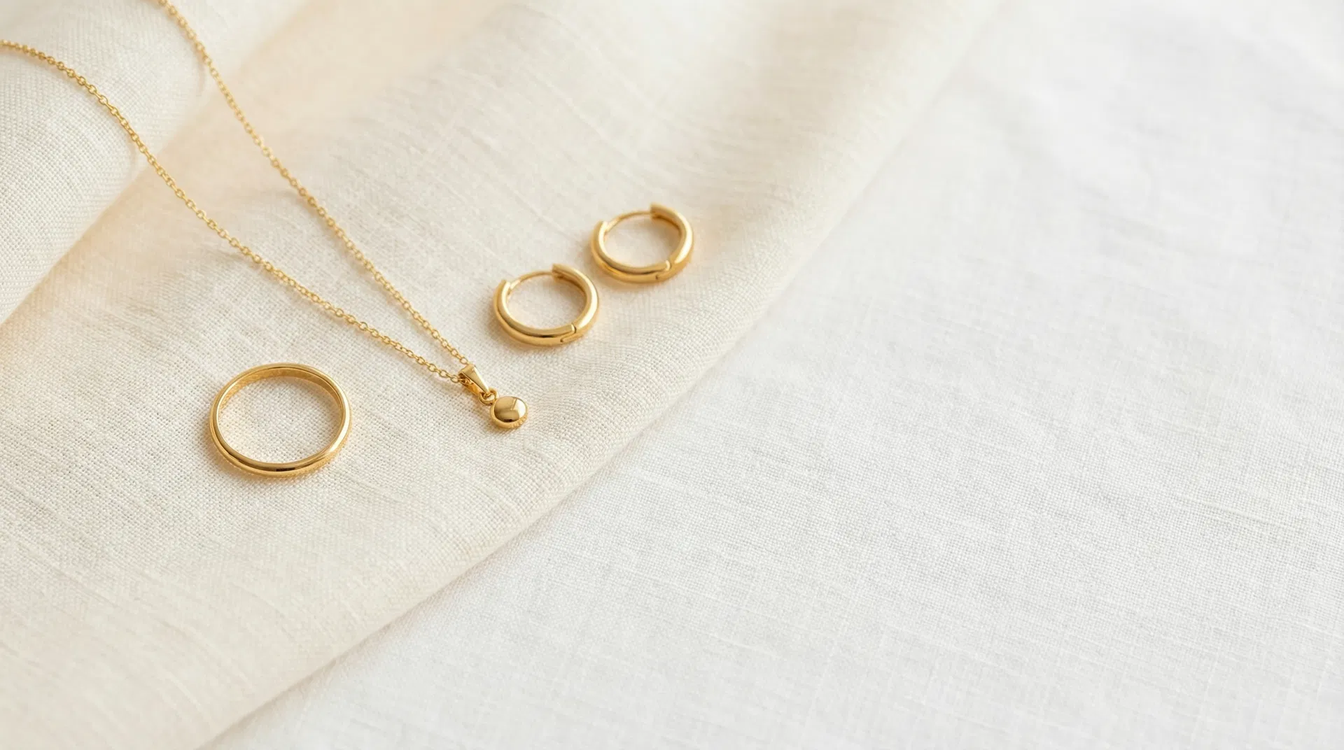 Gold-plated fine jewellery ring, necklace and earrings on white linen