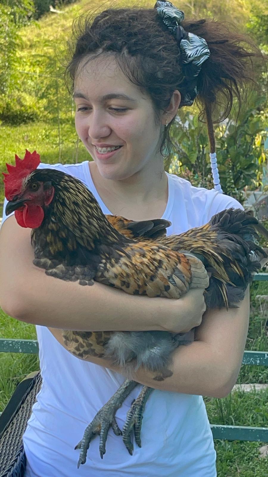 Gema holding a rooster in the garden