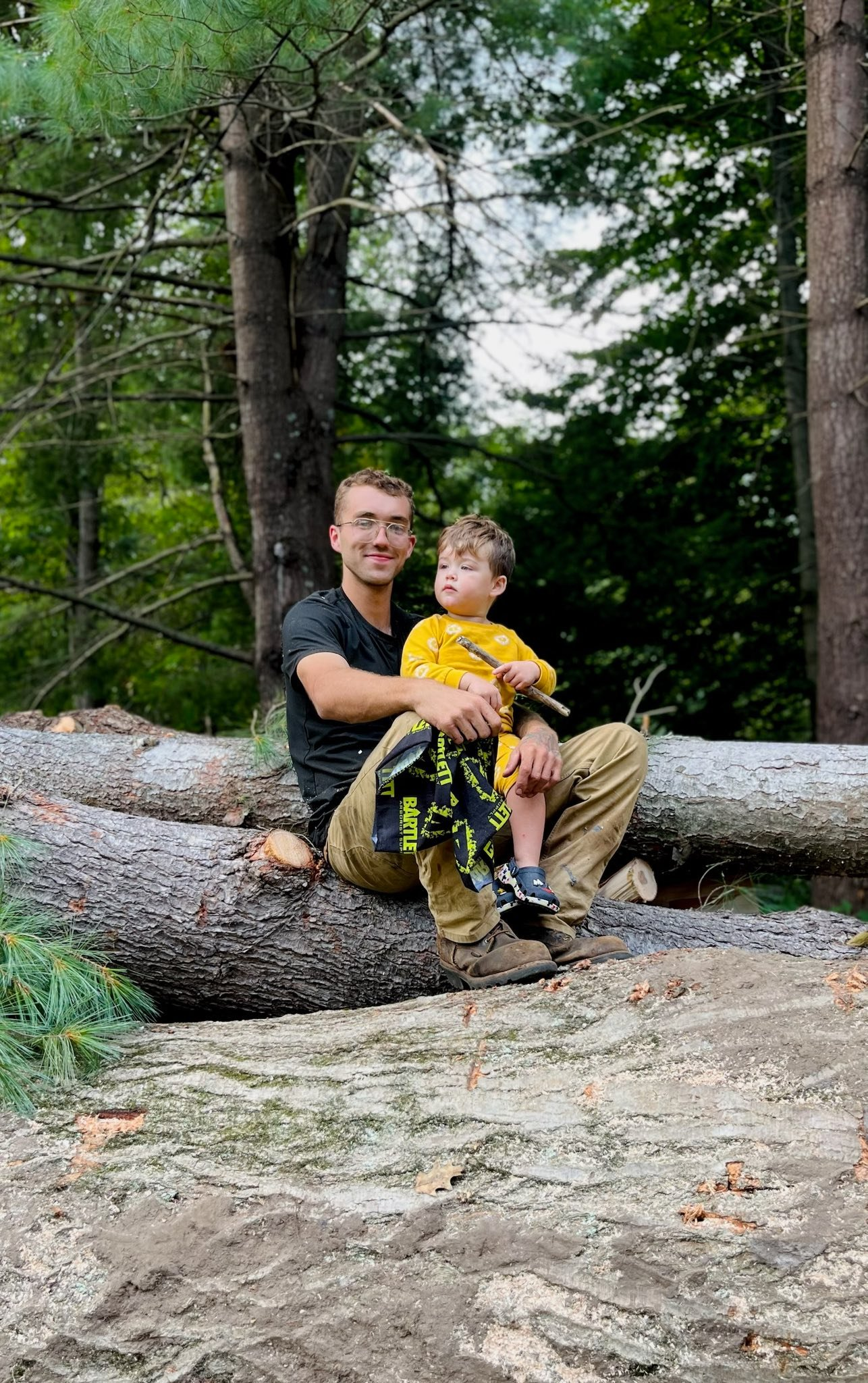 Jacob, owner of Broken Limb Tree Service, with his son sitting on a fallen tree in Bay City, Michigan